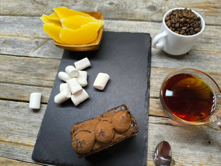 tender juicy tiramisu cake lies on a granite board next to marshmallows and a white cup with coffee beansの写真素材