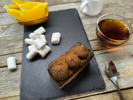 tender juicy tiramisu cake lies on a granite board next to pineapple pieces, marshmallows and a white cup with coffee beansの写真素材