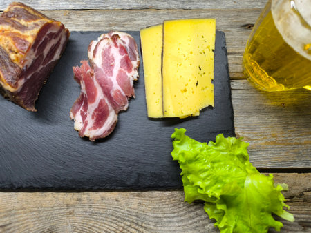 juicy sliced ââpiece of dried meat on a cutting board, next to it green salad leaves, cheese and a glass of beerの写真素材