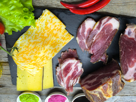 juicy sliced ââpiece of dried meat on a cutting board, next to it green salad leaves, cheese and a glass of beerの写真素材