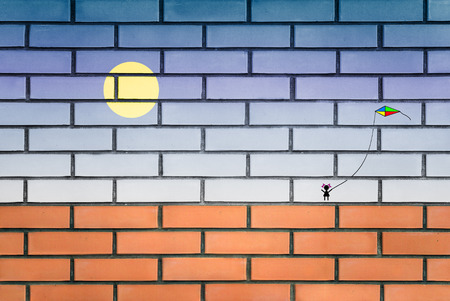 The photo of a red brick on which the sky, the sun and the little girl walking with a kite is drawnの写真素材