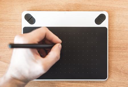 The photo of the graphic tablet on a wooden table close up on which draw a handの写真素材