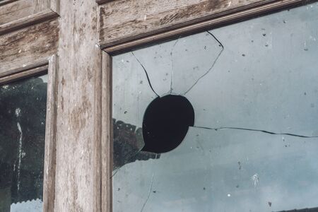 Photograph of an old wooden window on the street with broken glass with a hole
