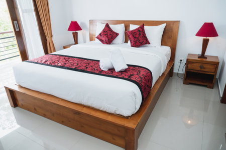 Photograph of bright white bedroom with wooden bed, white mattress and red pillowsのeditorial素材