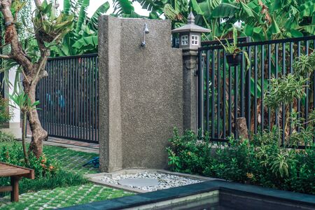 Photo of a summer outdoor shower in the backyard with green grass, trees and a metal fenceの写真素材