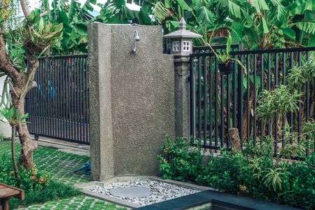 Photo of a summer outdoor shower in the backyard with green grass, trees and a metal fenceの写真素材