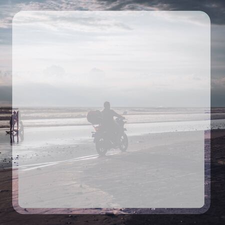 Photograph of a man riding a motorcycle on a beach with black sand and clouds in the skyの写真素材
