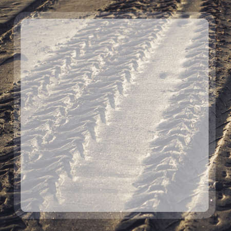 Photograph of a trace from car tires on wet sand with shadows from the sun