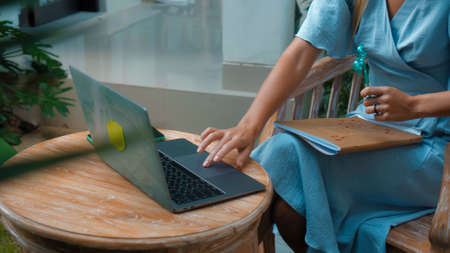 Photo of a young girl sitting at a wooden table and working behind a laptop in a green gardenの写真素材