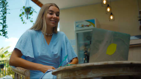 Photo of a young girl sitting at a wooden table and working behind a laptop in a green gardenの写真素材