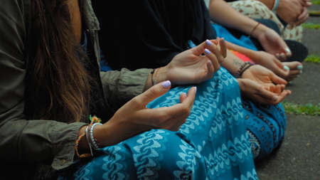 Photograph of the hands of people sitting in a lotus pose at an Indonesian ceremony handed over by aromotic sticks and baskets with flowersの写真素材