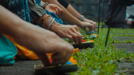 Photograph of the hands of people sitting in a lotus pose at an Indonesian ceremony handed over by aromotic sticks and baskets with flowersの写真素材