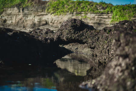 Photograph of an underwater marine colored ship with high cliffs in a sea tide of water with a reflection of the sky in the waterの素材 [FY310152853989]