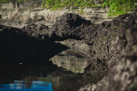 Photograph of an underwater marine colored ship with high cliffs in a sea tide of water with a reflection of the sky in the waterの写真素材