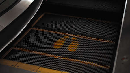 Black staircase escolator in a shopping center with a footprint sign for keeping a social distance