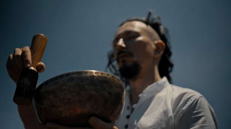 A young Asian guy playing Tibedt singing copper cups on a viewing mountain in nature