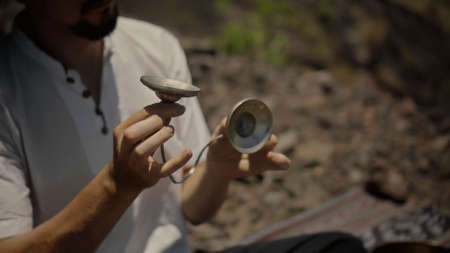 A young Asian guy playing Tibedt singing copper cups on a viewing mountain in nature