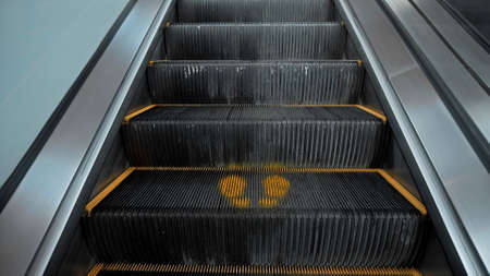Black staircase escolator in a shopping center with a footprint sign for keeping a social distance
