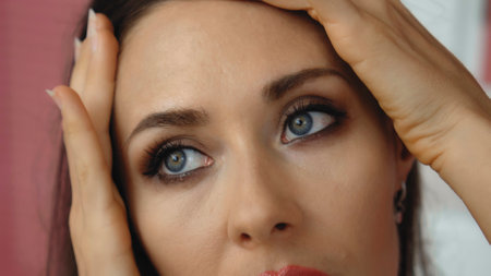Young and beautiful European girl close-up touches the skin of the face with tender hands and...