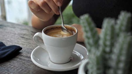A young European girl sits at a table in a public place with a cup of coffee on a wooden tableの写真素材