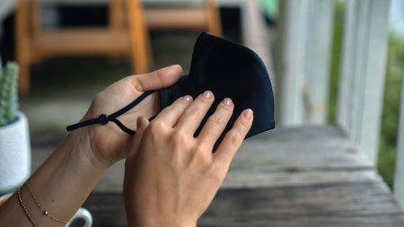 A young European girl sits at a table in a public place and holding a black protective mask with her handsの写真素材
