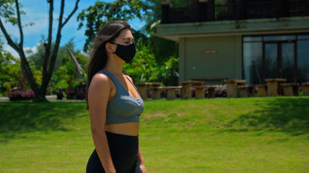 Young European brunette girl practices alone yoga in nature wearing a black protective mask on her faceの写真素材