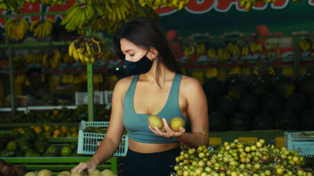 A young European girl in a black protective mask buys organic fruits in a storeの写真素材