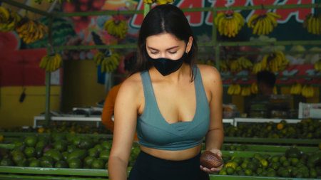 A young European girl in a black protective mask buys organic fruits in a storeの写真素材