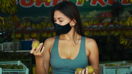 A young European girl in a black protective mask buys organic fruits in a storeの写真素材