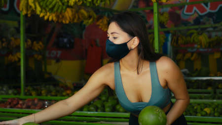 A young European girl in a black protective mask buys organic fruits in a storeの写真素材