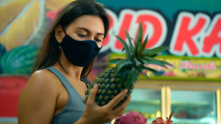 A young European girl in a black protective mask buys organic fruits in a storeの写真素材