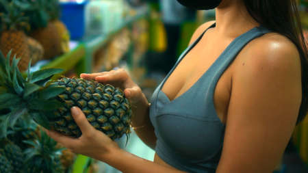 A young European girl chooses organic fruits in a store holding a pineapple in her handの写真素材