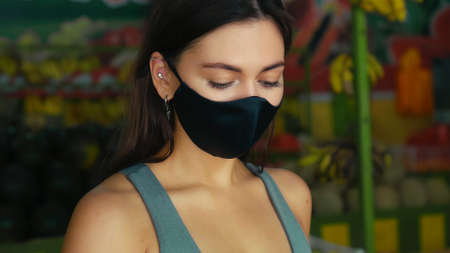 A young European girl in a black protective mask buys organic fruits in a storeの写真素材