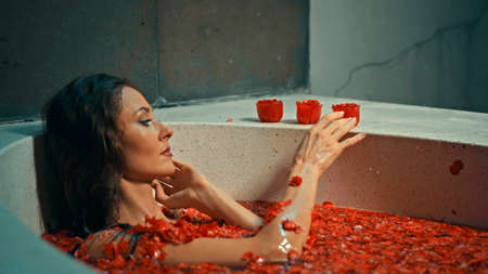 Young European girl long-haired brunette lies in the bathroom with red flowers on spa procedureの写真素材