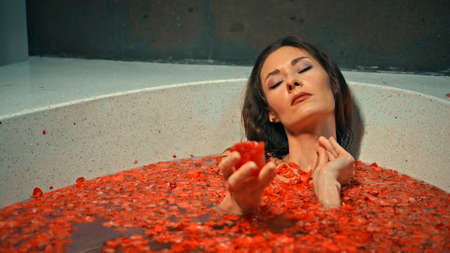 Young European girl long-haired brunette lies in the bathroom with red flowers on spa procedureの写真素材