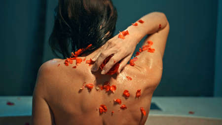 Young European girl long-haired brunette sits in the bathroom with red flowers on a spa procedure with soap in the shape of a roseの写真素材
