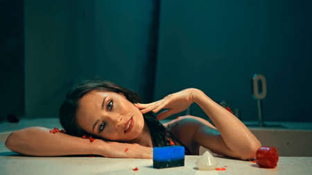 Young European girl long-haired brunette sits in the bathroom with red flowers on a spa procedure with soapの写真素材