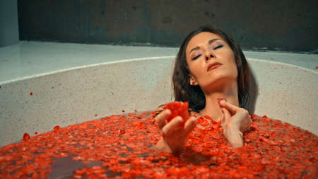 Young European girl long-haired brunette lies in the bathroom with red flowers on spa procedureの写真素材
