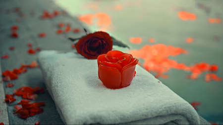 Red rose soap standing on a towel outside the pool with flower petalsの写真素材