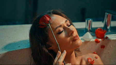 Young European girl long-haired brunette lies in the bathroom with red flowers on spa procedureの写真素材