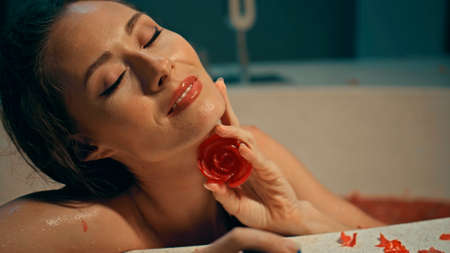 Young European girl long-haired brunette sits in the bathroom with red flowers on a spa procedure with soap in the shape of a roseの写真素材