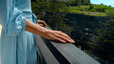 A young girl stands in the summer on a balcony in a blue dress clouding on a railingの写真素材