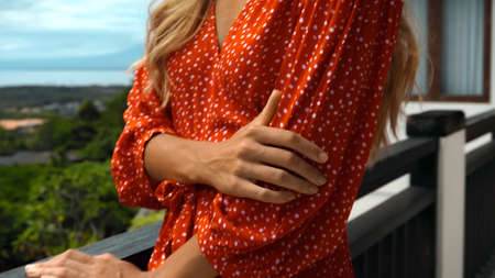 A young girl long hair blonde touches a red dress with a white dots with her hand standing on a balconyの写真素材