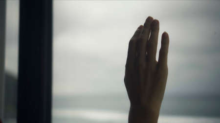 young European girl standing in a house behind a window and touching a wooden frame with her hand on a red dressの写真素材