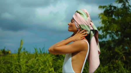 Young European brunette girl with a towel on her head in the backyard with a green garden on the backgroundの写真素材