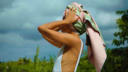 Young European brunette girl with a towel on her head in the backyard with a green garden on the backgroundの写真素材