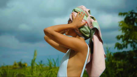 Young European brunette girl with a towel on her head in the backyard with a green garden on the backgroundの写真素材