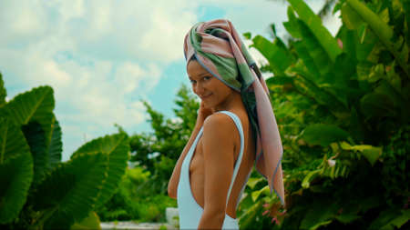 Young European brunette girl with a towel on her head in the backyard with a green garden on the backgroundの写真素材