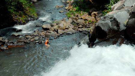 Picture of waterfall with rocks among tropical jungle with green plants trees and river. A girl lies at a waterfall after an unsuccessful jump from a waterfallの写真素材