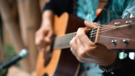 The young man plays hands and on a classic acoustic wooden guitar on the street using a microphoneの写真素材